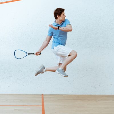 Sportsman in polo shirt jumping while playing squash in four-walled court